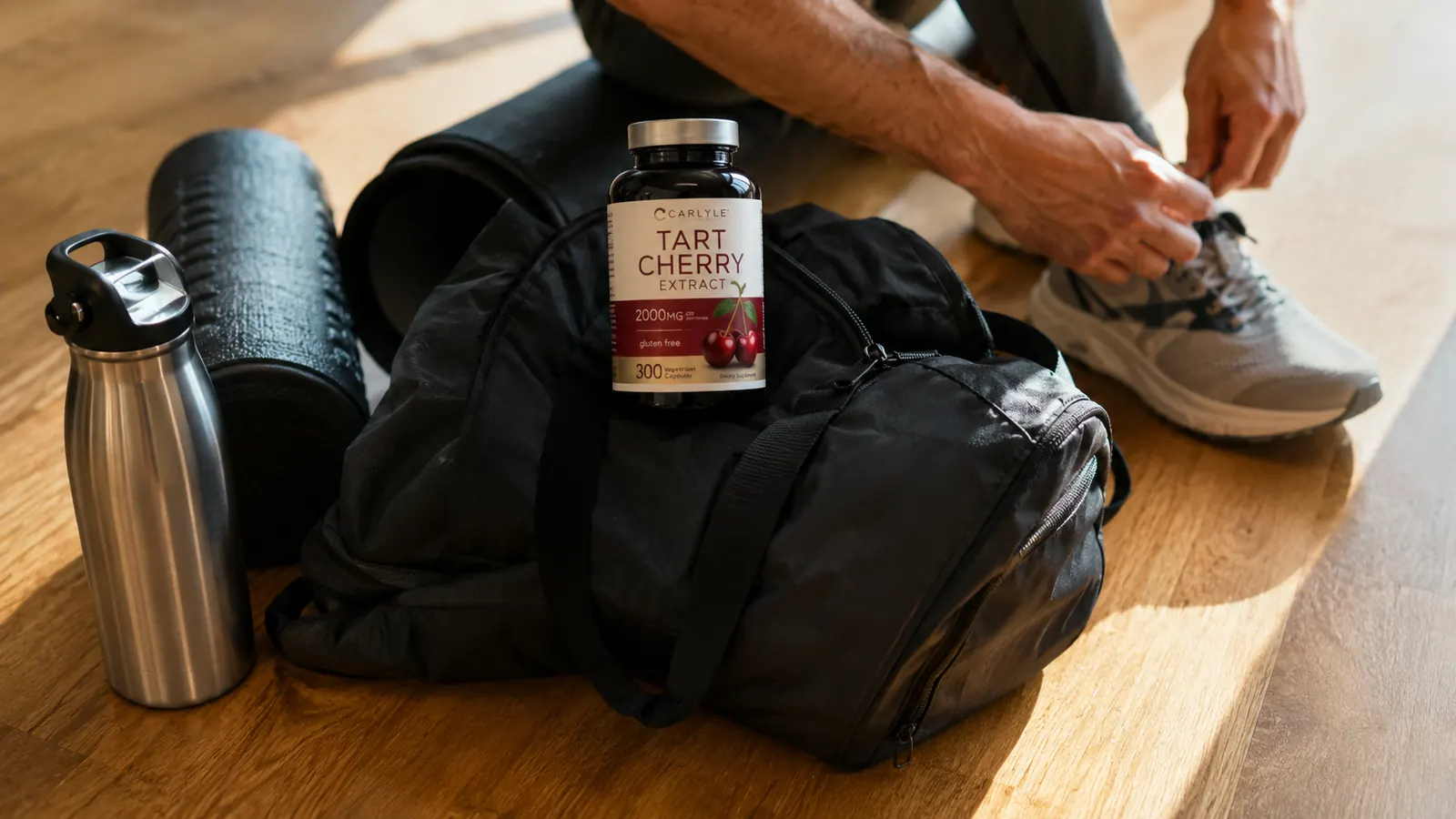 Carlyle tart cherry capsule bottle on a gym bag next to a water bottle and a foam roller on a wood floor