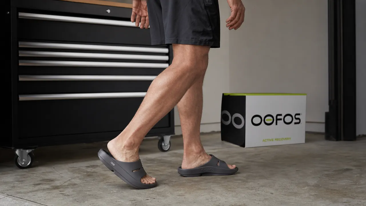 Person wearing OOFOS slides walking on a concrete garage floor, viewed from the knees down