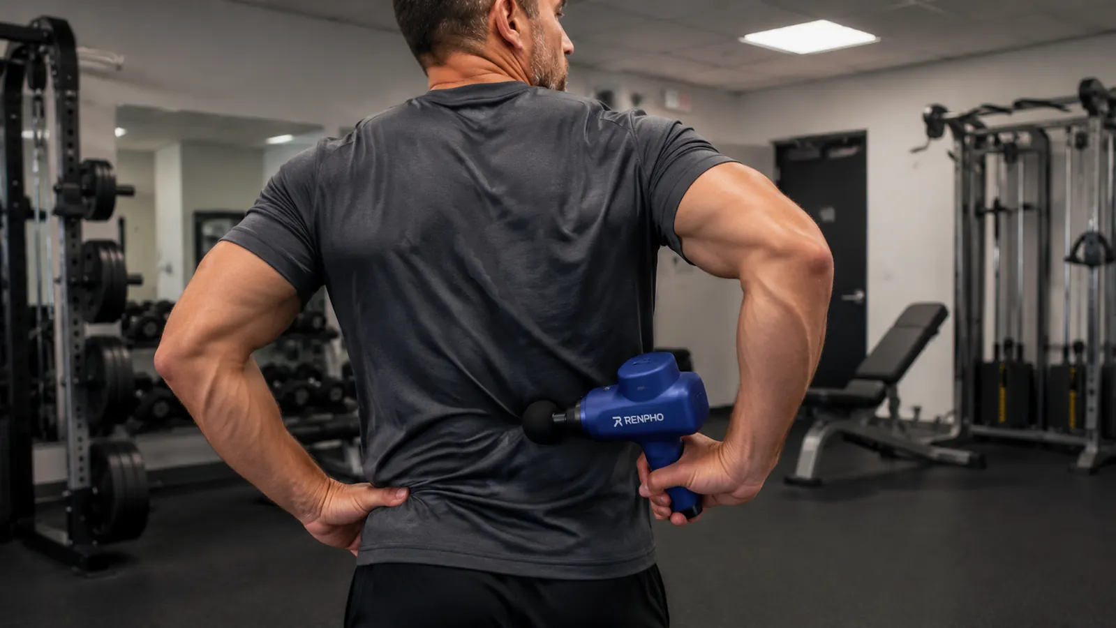 Person using the RENPHO massage gun on their lower back after a workout, standing in a gym
